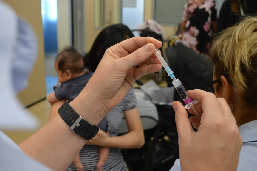 A nurse preps a syringe ahead of an immunisation