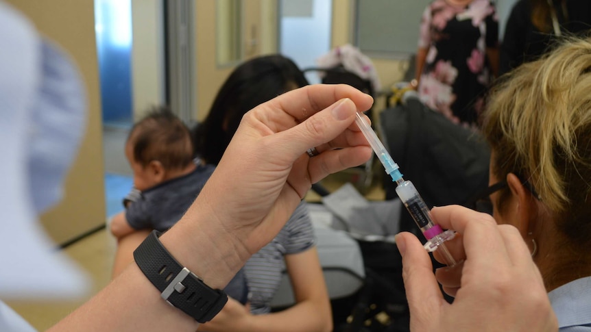 A nurse preps a syringe ahead of an immunisation