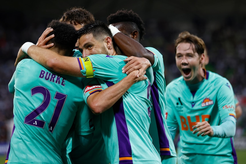 Perth Glory players huddle together celebrating a goal.