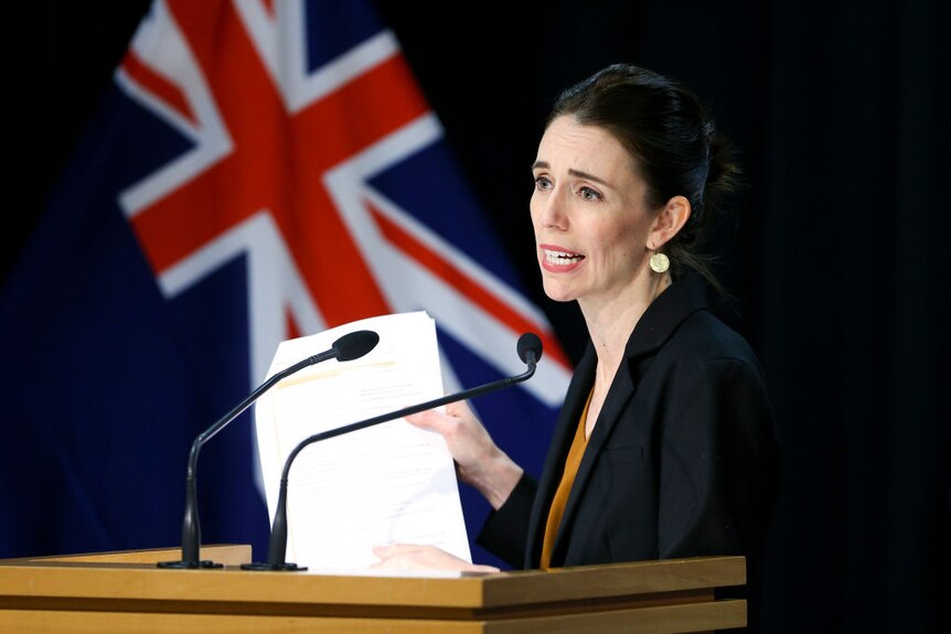 Jacinda Ardern holds up piece of paper while speaking to media at press conference.