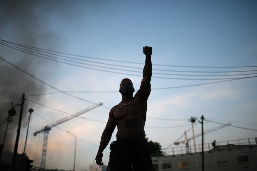 A protester raises his fist as smoke rises in the street behind him.