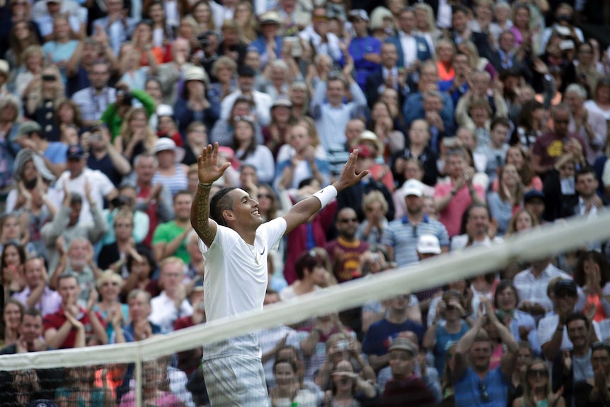 Nick Kyrgios raises his arms in triumph dressed in all white.