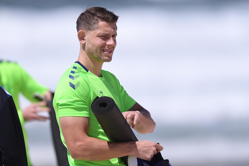 James Tarkowski holds a yoga mat on Bondi Beach