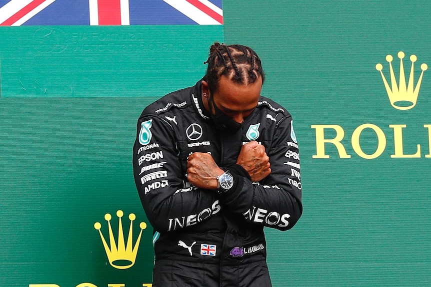 Lewis Hamilton bends his head forward and crosses his hands in front of his chest