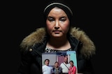 Fatimah Abdulghafur holds a family portrait against a black background.