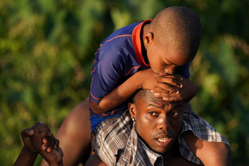 A man carries a young boy on his shoulders as migrants cross Rio Grande river.