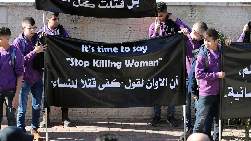 Teenagers hold banners in English and Arabic denouncing violence against women at the funeral of Aiia Maasarwe.