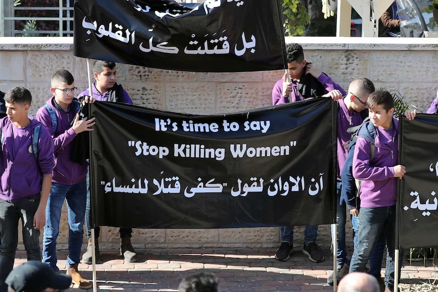 Teenagers hold banners in English and Arabic denouncing violence against women at the funeral of Aiia Maasarwe.