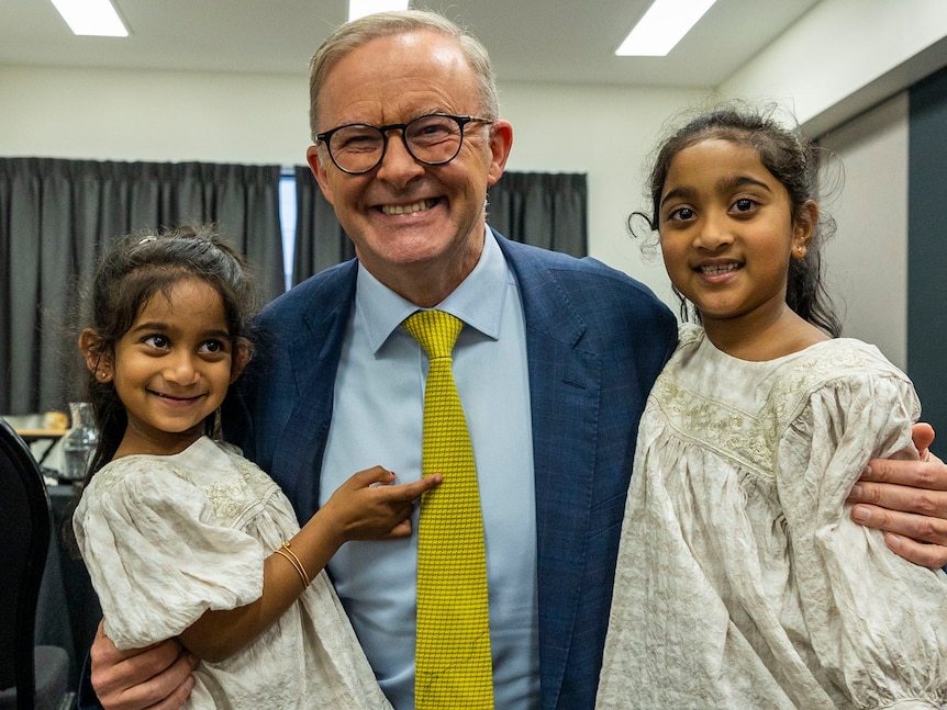 A smiling man with a blue suit hugs two little smiling girls. 