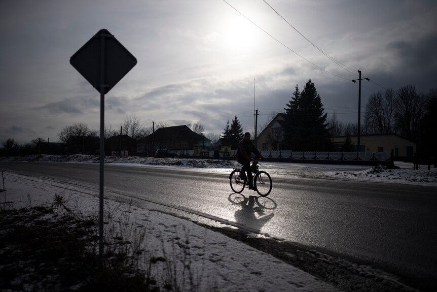 The silhouette of a man riding a bike along a snowy road. 