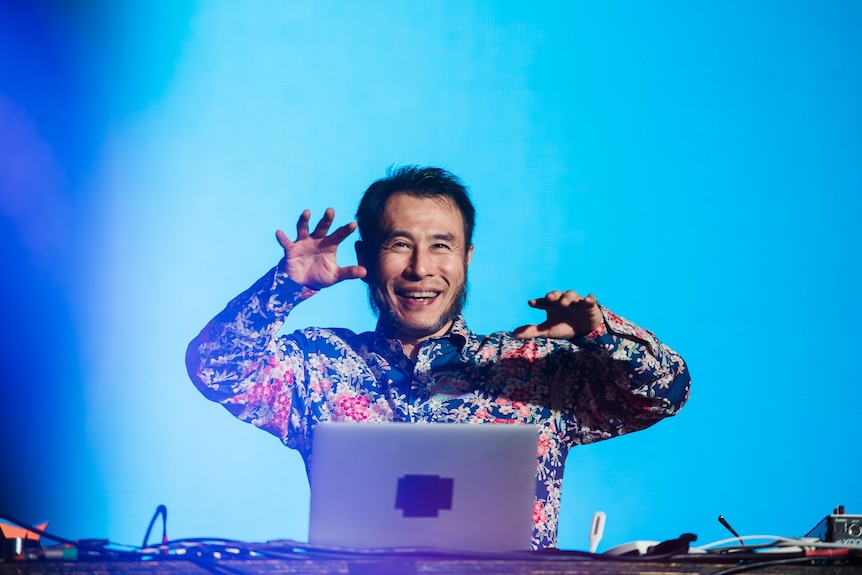 Japanese producer Soichi Terada smiles, hands hovering over his laptop onstage at Golden Plains festival 2023