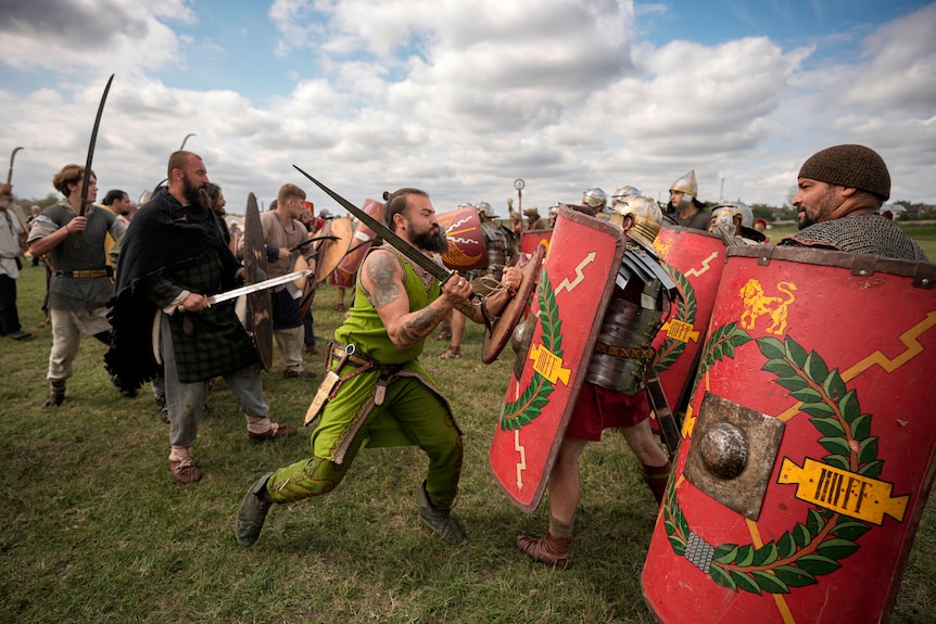 men with swords charge forward against men carrying red shields