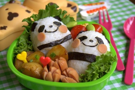Two panda bears made of rice and seaweed sitting in a green bowl filled with lettuce and other food.