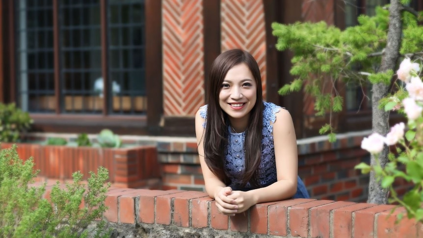 Woman leans forward with arm resting on a red brick fence.