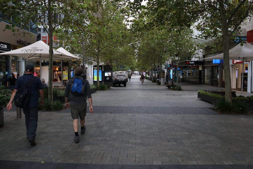 Two people walk down an empty Perth CBD road.