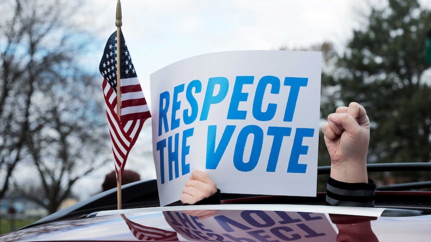 You see a hand holding a sign out of a car saying Respect the Vote, alongside a raised fist and US flag.