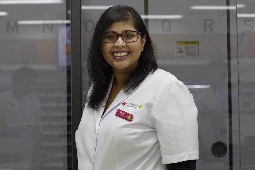 A woman smiles at the camera in a pharmacy