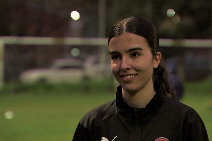 Sara Marta looks off to one side of the camera with a smile on her face, wearing a black jacket