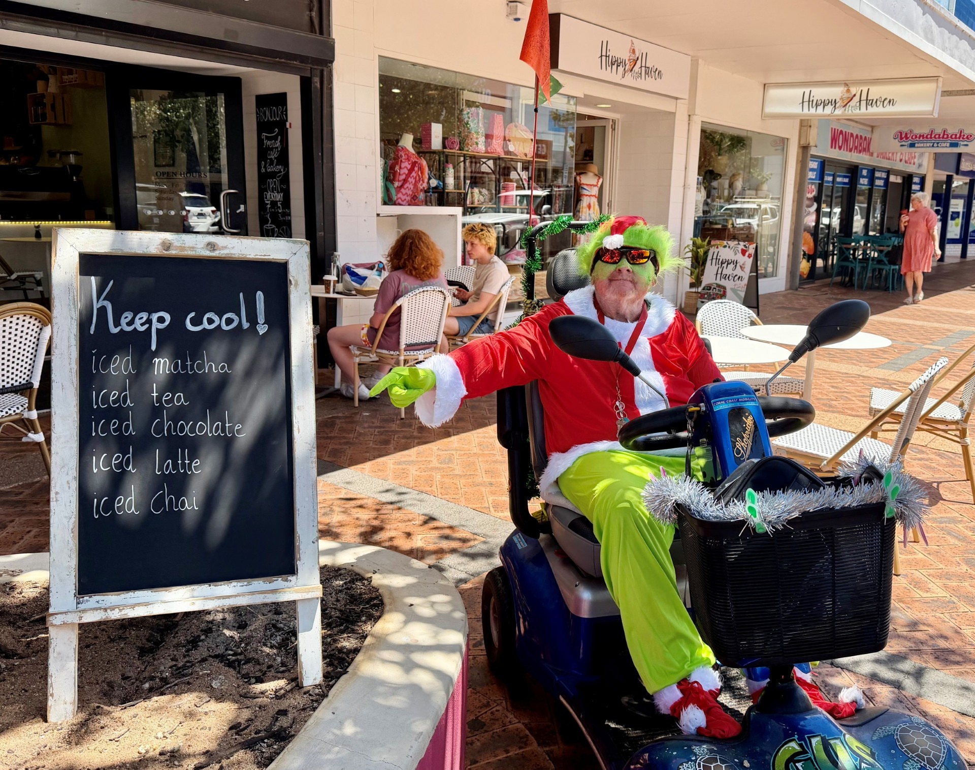 Um homem vestido com um terno grinch senta-se em uma cadeira em um shopping center