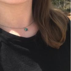 A brunette woman wearing a solver necklace with a green stone pendant.