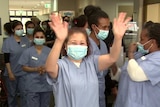 nurses wearing surgical masks smiling and clapping in a hallway