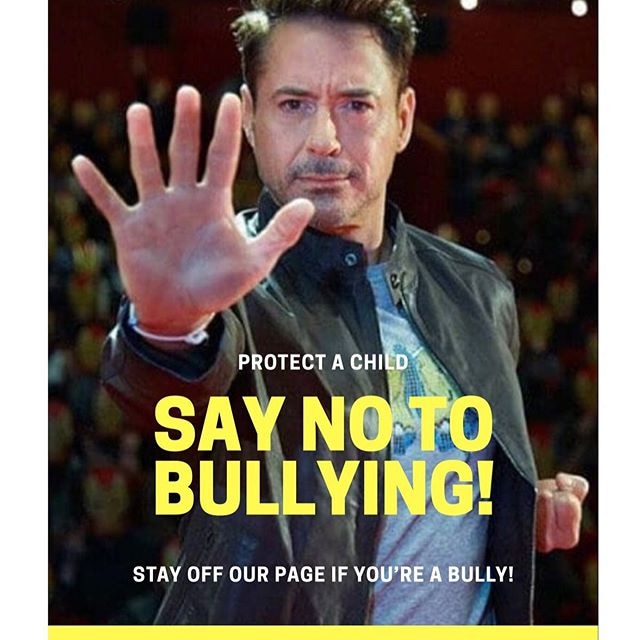 A man in a leather jacket holds his right palm up and left fist near his hip behind a banner reading "say no to bullying!"
