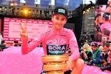 Australia's Jai Hindley sits on a pink runway wearing a pink jersey, holding a golden trophy after the Giro d'Italia.
