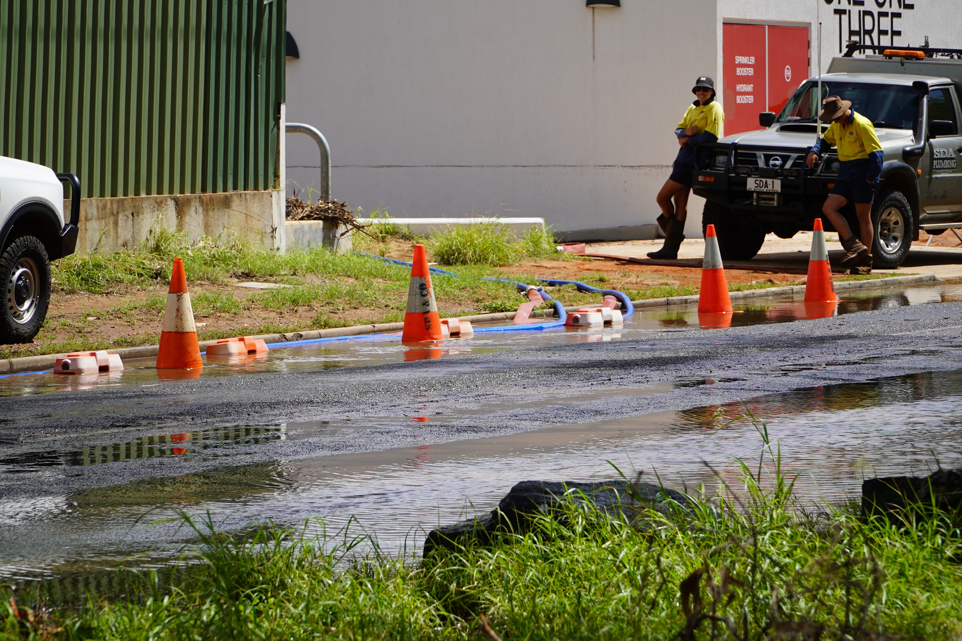 Dois homens com camisas amarelas de alta visibilidade estão ao lado de um carro na beira de uma estrada inundada marcada com chapéus de bruxa.