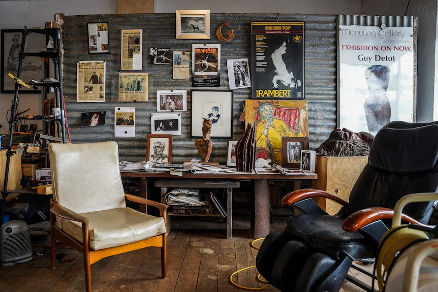 Old photographs, posters and magazine articles line a corrugated iron wall inside a gallery space.