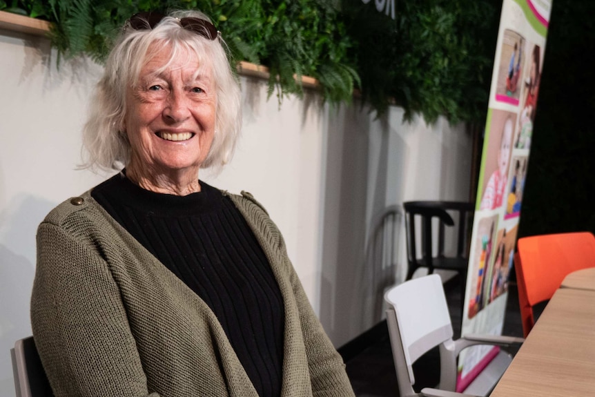 Older woman sitting at table, smiling at camera