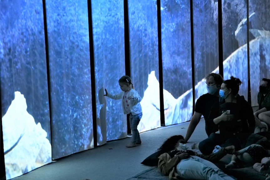 A girl touches a screen on stage that has vivid earthy imagery