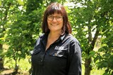 Joanne Fahey stands wearing a black shirt among apple trees in her orchard.