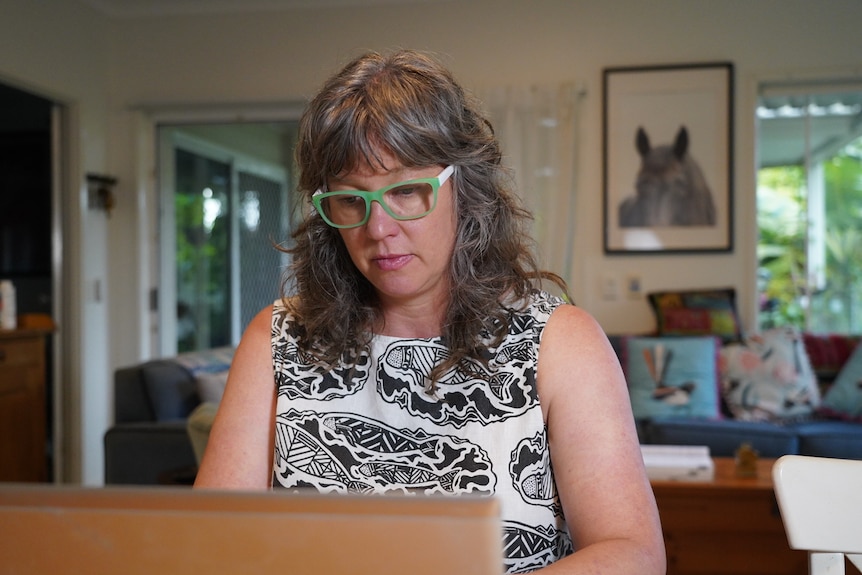 Caroline Page, wearing green reading glasses and a patterned top, types at a computer.