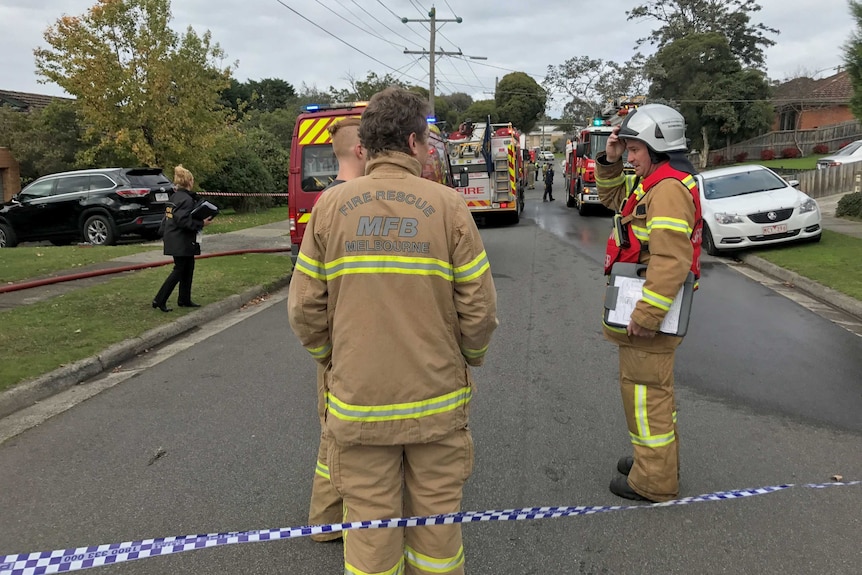 Fire crews stand on a street near their fire trucks where there was a house fire in Bundoora.