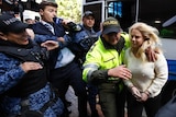 A police officer escorts Cassie Sainsbury past media and into the court house.