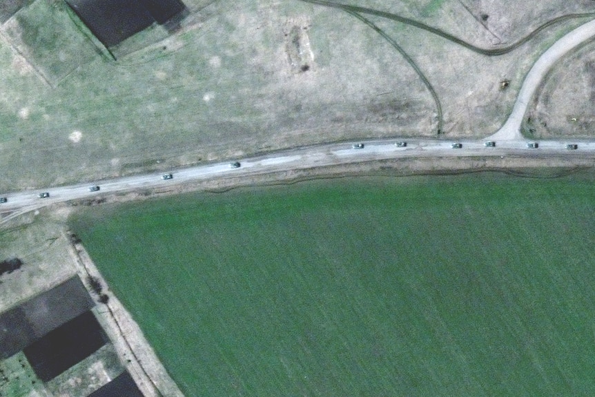 На спутниковом снимке виден ряд автомобилей на дороге, окруженной лугами.