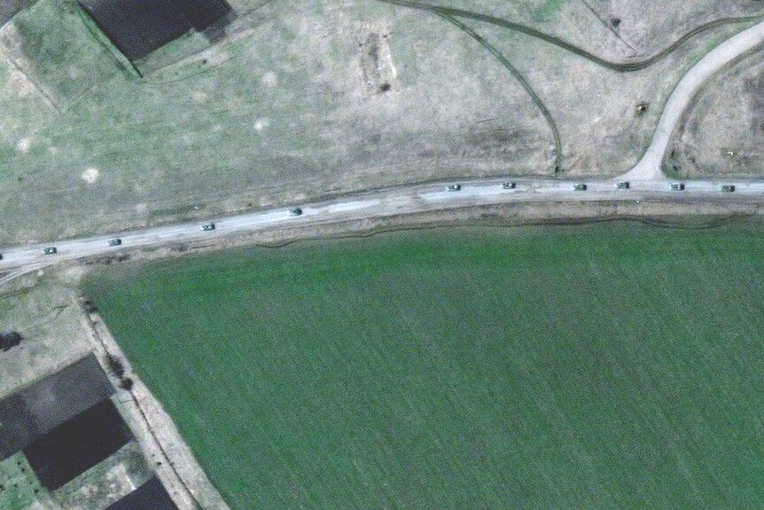 A satellite image of vehicles on a road surrounded by green paddocks.