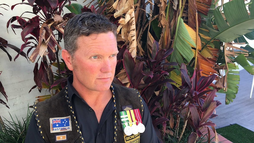 Derek Pyrah, 43, with three medals pinned to his vest, gazes off camera pensively.