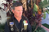 Derek Pyrah, 43, with three medals pinned to his vest, gazes off camera pensively.