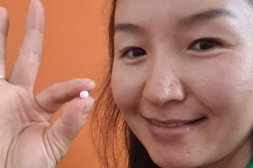 Close up of woman's face holding up a small white pearl pinched in her forefinger and thumb 