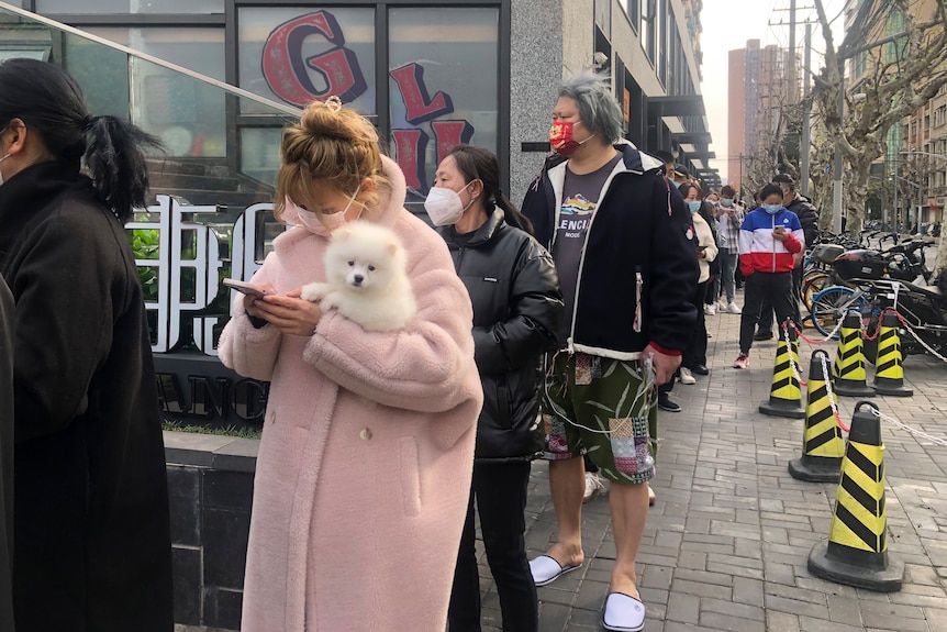 a girl is waiting in line with a white puppy in hear arms