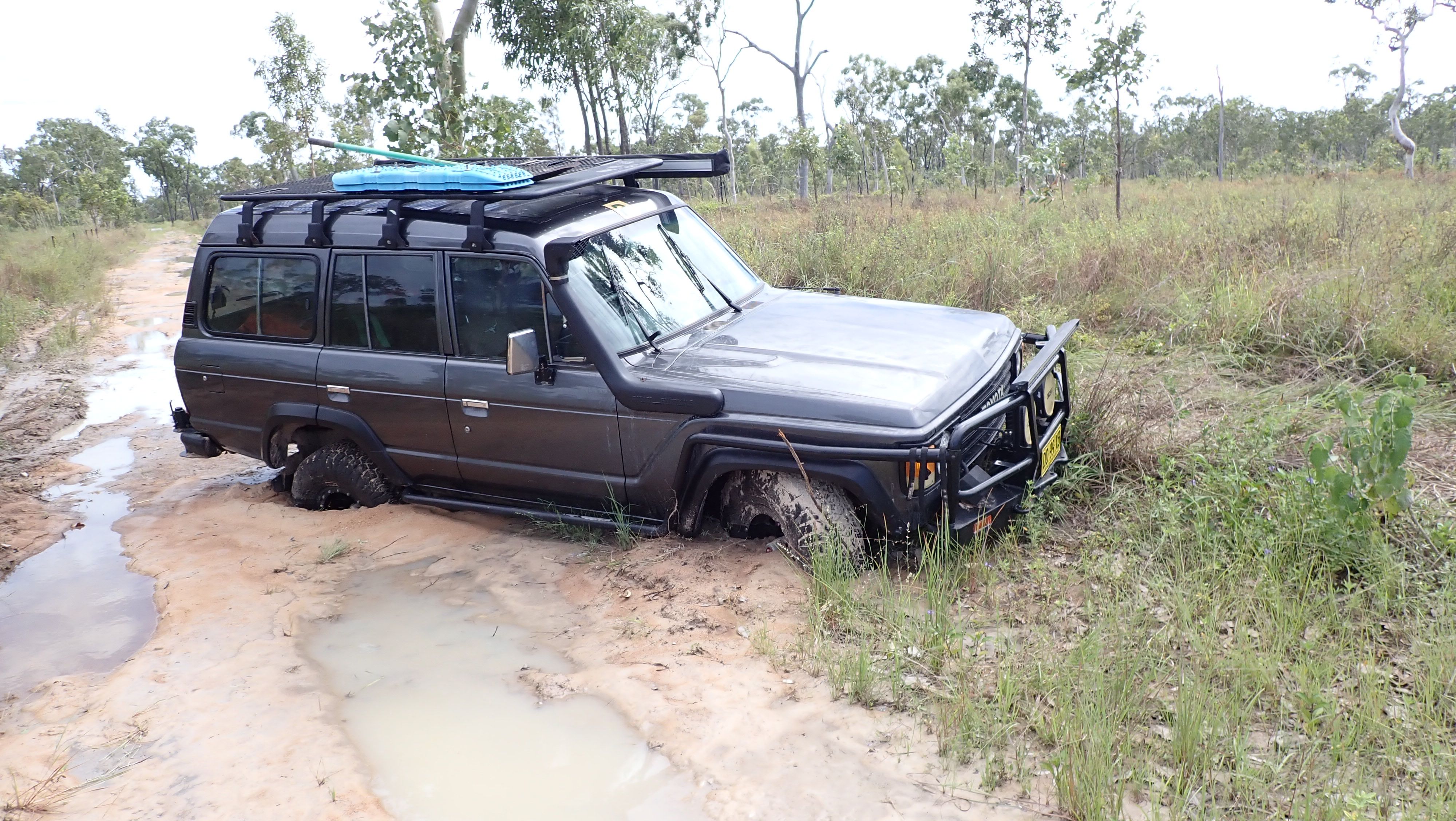 A four wheel drive has two wheels submerged in mud. It's front bumpber is touching the ground.