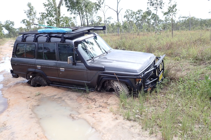 A four wheel drive has two wheels submerged in mud. It's front bumpber is touching the ground.