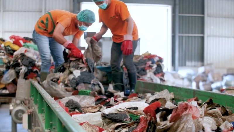 Two people in orange t-shirts sort through paper waste.