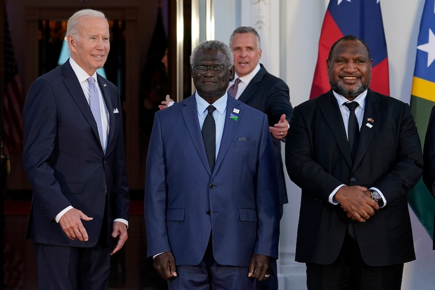 Joe Biden stands next to Manasseh Sogavare, who stands beside James Marape as they pose for a photo near flags.