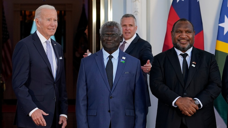 Joe Biden stands next to Manasseh Sogavare, who stands beside James Marape as they pose for a photo near flags.