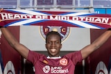 Garang Kuol holds up a Heart of Midlothian scarf while standing in the tunnel at the home ground of the football club.
