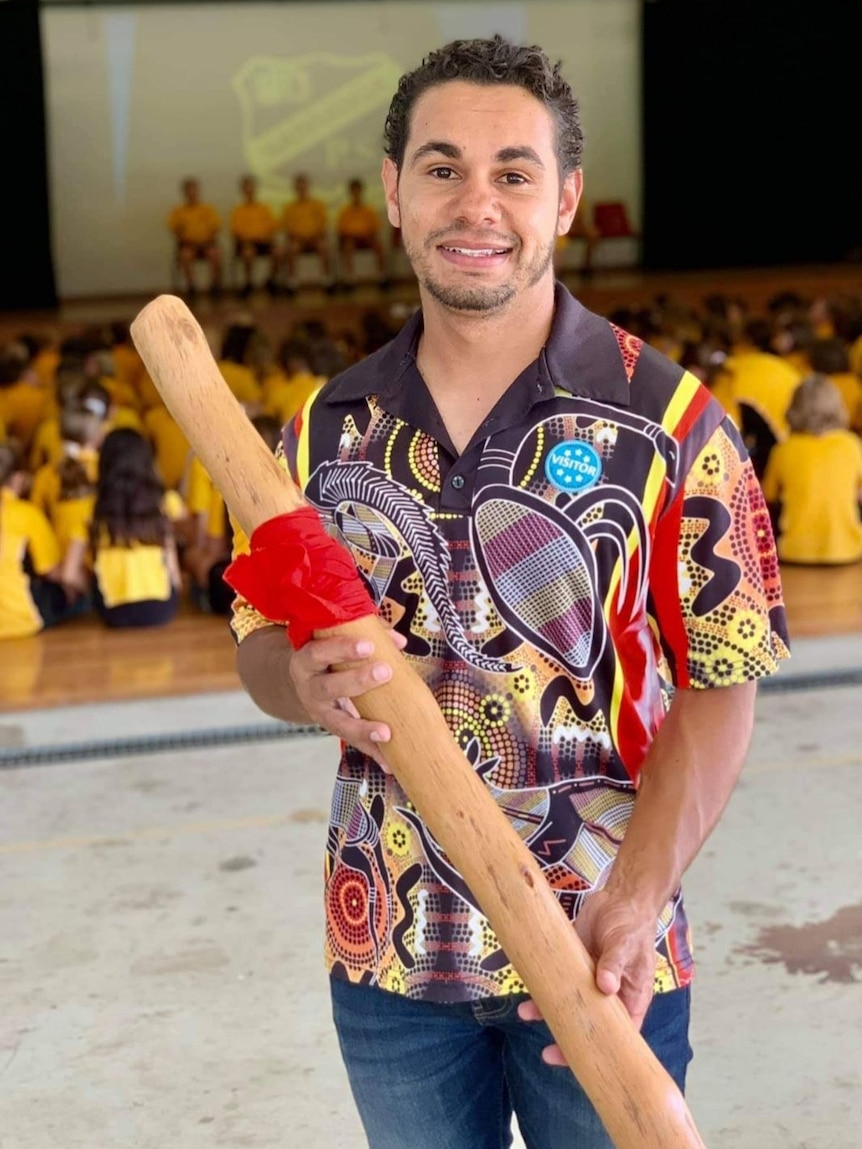 Manduway smiles at the camera while holding a didgeridoo. 