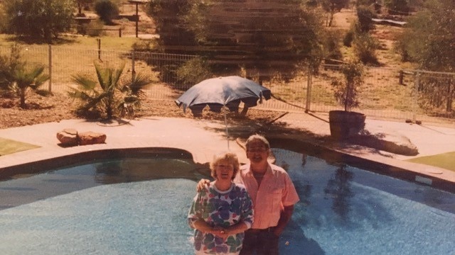 An older photo of a couple posing in front of an Australia-shaped pool.
