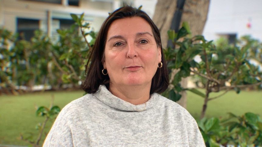 A woman with short brown hair stands in front of a garden bed